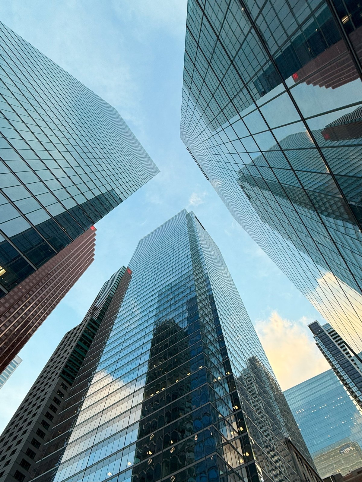 Low angle view of modern glass skyscrapers reflecting the sky and surrounding city buildings. Contemporary urban skyline in a business district.